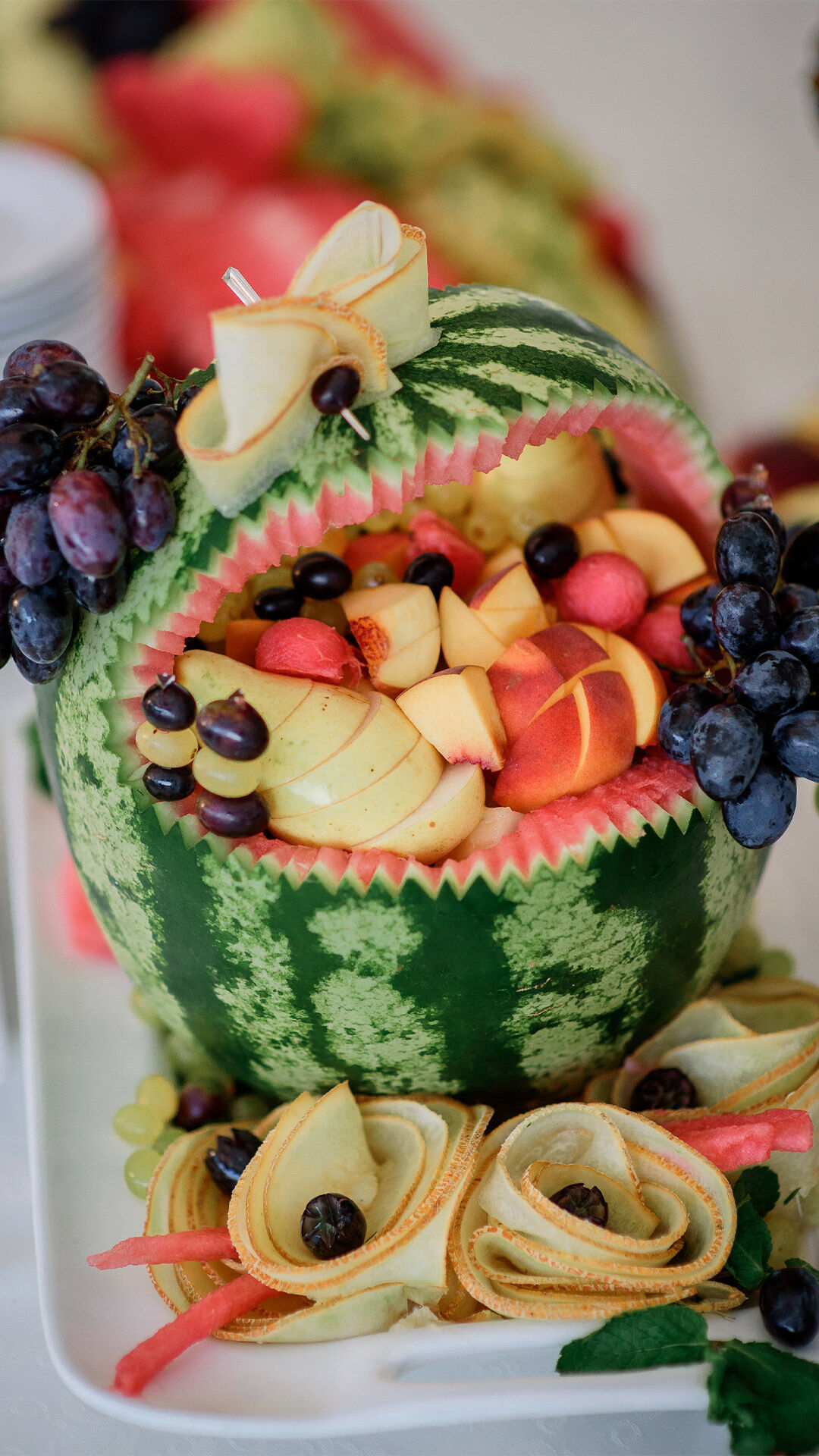 Creative watermelon fruit basket carved and filled with apple slices, grapes, and melon balls, decorated with ribbon-like fruit garnishes for a wedding display